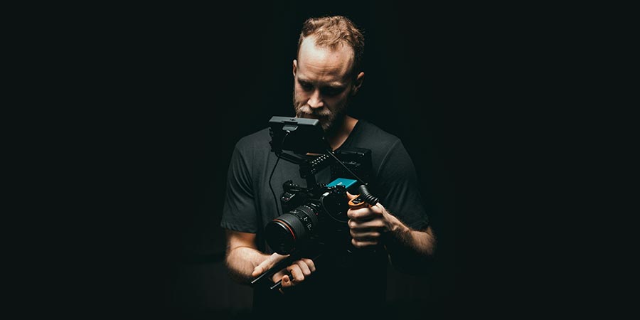 a man wearing a black t-shirt holding a black camera in the dark